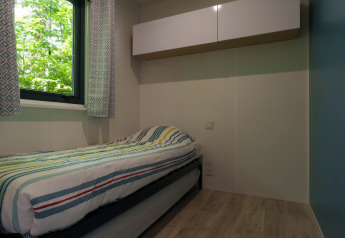 Habitación luminosa con cama individual, cortinas estampadas y armario superior en un lodge acogedor.