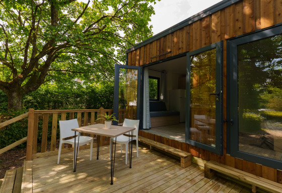 Terraza exterior en una cabaña de madera con mesa, sillas y puertas de cristal abiertas al jardín.
