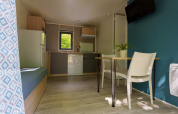Interno di lodge moderno con cucina, tavolo da pranzo, due sedie bianche, parete blu e luce naturale.