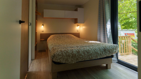 Cozy lodge bedroom with a double bed, soft lighting, modern decor, and view of the wooden terrace.