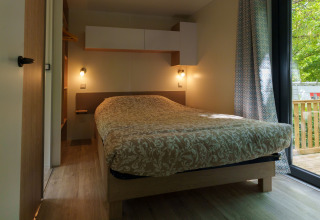 Chambre confortable d’un lodge avec lit double, éclairage doux, déco moderne et vue sur la terrasse boisée.