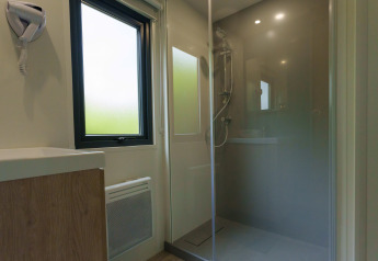 Modern lodge bathroom with glass shower enclosure, large frosted window, and sink with wood vanity below.