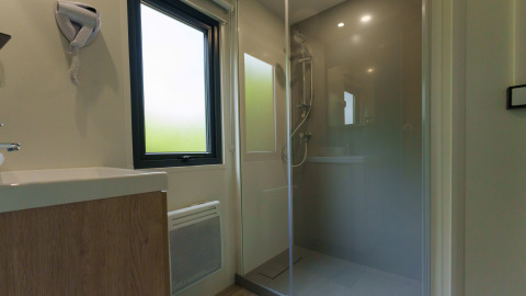 Bagno moderno in un lodge con doccia in vetro, ampia finestra satinata e lavabo con mobile in legno.