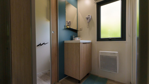 Bagno in un lodge con specchio, lavandino, mobile in legno, finestra, stufa a parete e asciugacapelli.