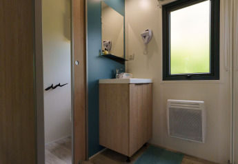 Bagno in un lodge con specchio, lavandino, mobile in legno, finestra, stufa a parete e asciugacapelli.