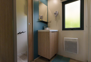 Bathroom in a lodge with mirror, sink, wooden cabinet, window, wall-mounted heater, and hairdryer.