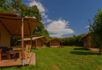 Foto de las tiendas safari Slow Lodge en Camping Seasonova Vittel, Francia, rodeadas de naturaleza y árboles.