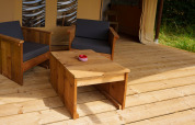 Zona de estar exterior de madera con cojines negros en una tienda safari Slow Lodge en Camping Seasonova Vittel, Francia.