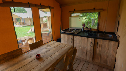 Cocina y mesa de comedor dentro de una tienda safari en Slow Lodge, Camping Seasonova Vittel, Francia, con vista al jardín.