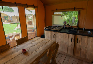 Cocina y mesa de comedor dentro de una tienda safari en Slow Lodge, Camping Seasonova Vittel, Francia, con vista al jardín.