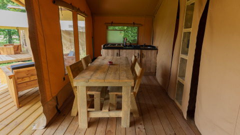 Interior view of the Slow Lodge safari tent at Camping Seasonova Vittel, France, with wood furniture and kitchen.