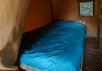 Binnenzicht van een bed met blauw beddengoed in een safaritent bij Slow Lodge, Camping Seasonova Vittel, Frankrijk.