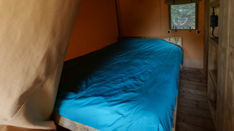 Vista interna di un letto con lenzuola blu in una tenda safari al Slow Lodge, Camping Seasonova Vittel, Francia.