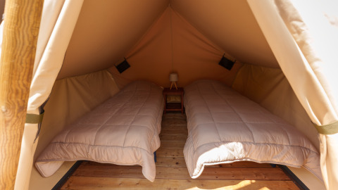 Vista interna di una tenda safari con due letti singoli, pavimento in legno e un piccolo comodino centrale.