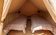 Vista interna di una tenda safari con due letti singoli, pavimento in legno e un piccolo comodino centrale.