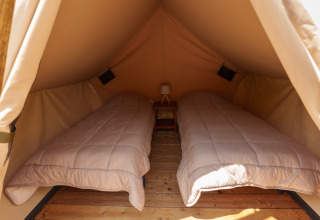Vue intérieure d'une tente safari avec deux lits simples, parquet en bois et une petite table de chevet centrale.