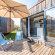 Udendørs terrasse ved Cottage Prestige med trædæk, parasol, blåt loungesæt og adgang til moderne køkken.