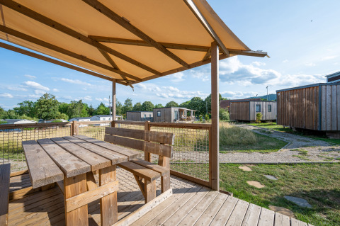 Wooden terrace with bench and table at Cottage Prestige, Camping Seasonova Les Portes d'Alsace, France, on a sunny day.