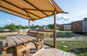 Wooden terrace with bench and table at Cottage Prestige, Camping Seasonova Les Portes d'Alsace, France, on a sunny day.