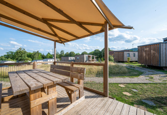 Wooden terrace with bench and table at Cottage Prestige, Camping Seasonova Les Portes d'Alsace, France, on a sunny day.