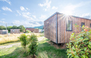 Vista soleada de la cabaña de madera Cottage Prestige en Camping Seasonova Les Portes d'Alsace, Francia, rodeada de naturaleza.