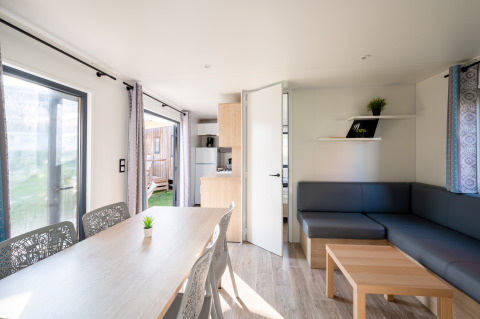 Bright interior of Cottage Prestige lodge at Camping Seasonova Les Portes d'Alsace, with table and sofa area.