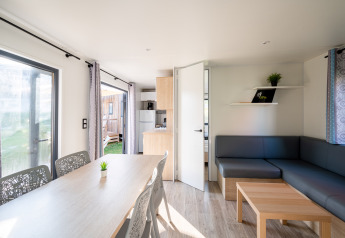 Bright interior of Cottage Prestige lodge at Camping Seasonova Les Portes d'Alsace, with table and sofa area.