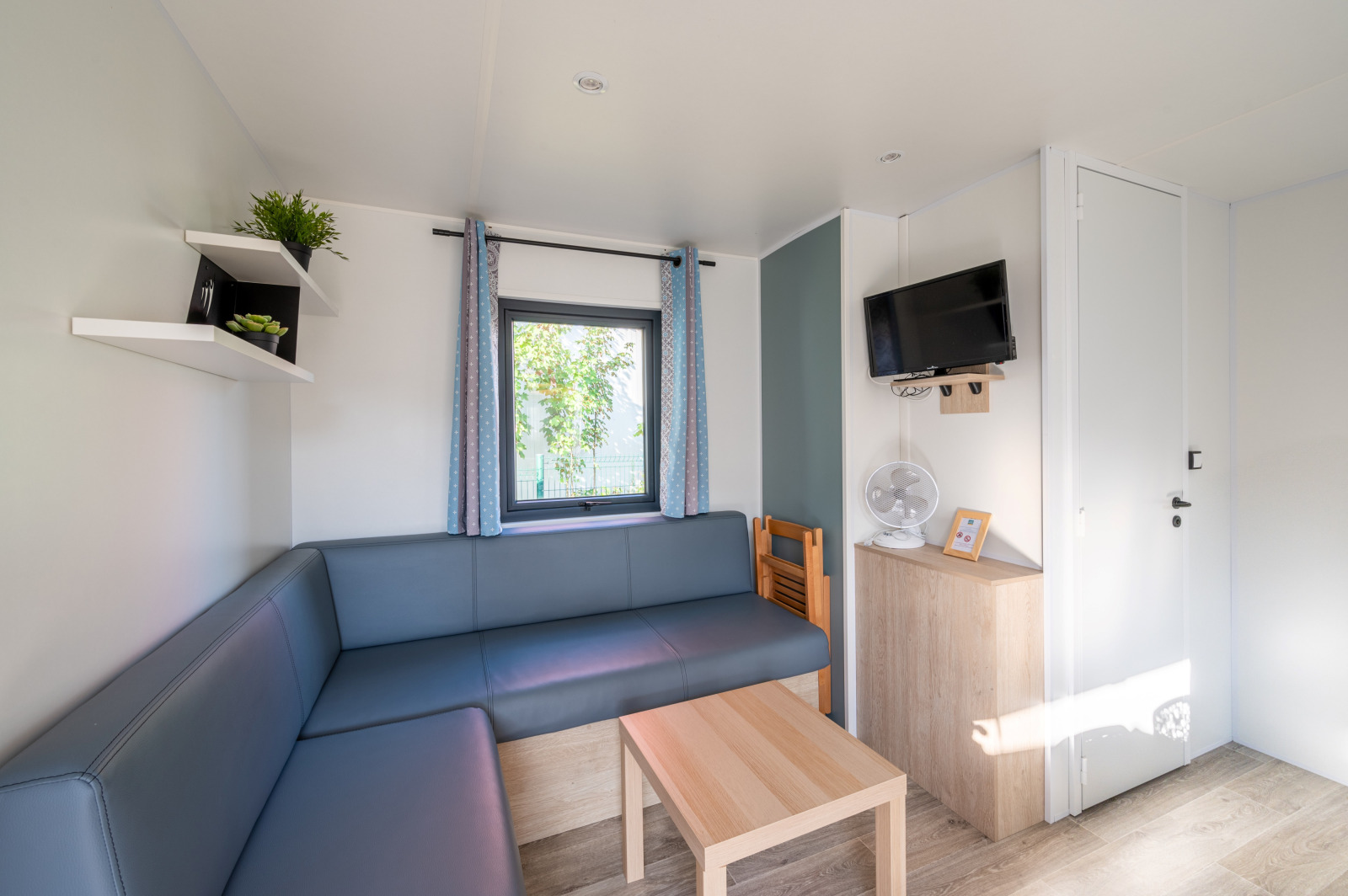 Lichte, moderne woonkamer in Cottage Prestige bij Camping Seasonova Les Portes d'Alsace met bank en tv.