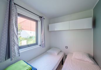 Værelse med to enkeltsenge, store vinduer med gardiner og moderne opbevaringsskabe på Camping Seasonova.