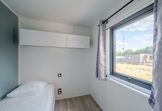 Moderna camera da letto con letto singolo, grande finestra e armadio bianco al Cottage Prestige in Francia.