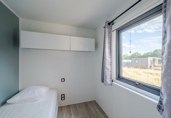 Moderna camera da letto con letto singolo, grande finestra e armadio bianco al Cottage Prestige in Francia.