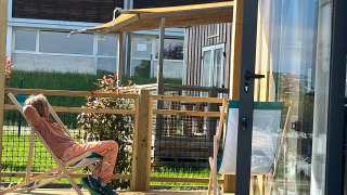 A person relaxes on a deck chair on the wooden terrace at Cottage Prestige lodge on a sunny day.