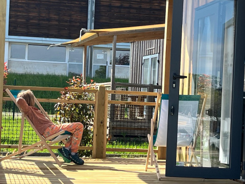 Una persona si rilassa su una sdraio sulla terrazza in legno del lodge Cottage Prestige in una giornata di sole.