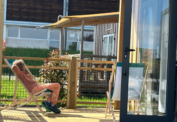 A person relaxes on a deck chair on the wooden terrace at Cottage Prestige lodge on a sunny day.