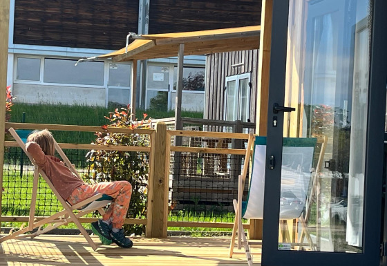 Una persona si rilassa su una sdraio sulla terrazza in legno del lodge Cottage Prestige in una giornata di sole.