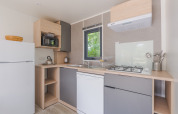 Modern kitchen in Cottage Prestige at Camping Seasonova Les Portes d'Alsace, France, with gas stove and fridge.