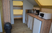 Safari tent interior with small kitchen, microwave, fridge, coffee maker, and wooden bunk beds in back.