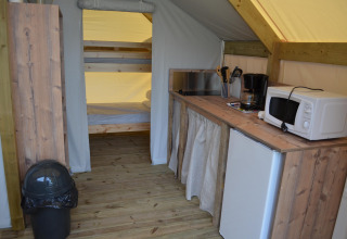 Binnenkant van een safaritent met keukenhoek, microgolfoven, koelkast, koffietoestel en stapelbedden achteraan.