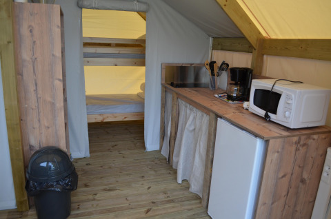 Interno tenda safari con cucina, microonde, frigo, macchina caffè e letti a castello in legno sullo sfondo.
