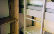 Interno di una tenda safari con letto a castello, cuscini bianchi e scaffale di legno accanto.
