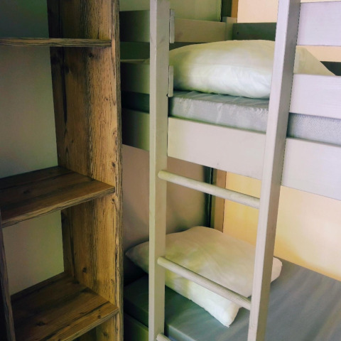 Interno di una tenda safari con letto a castello, cuscini bianchi e scaffale di legno accanto.