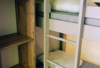 Binnenkant van een safaritent met stapelbed, witte kussens en houten rek naast het bed.