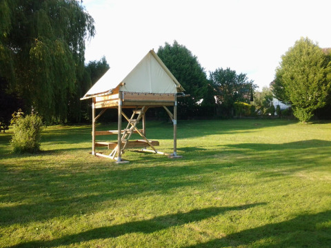 The Bivouac safari tent sits on a grassy field, surrounded by trees and basking in the afternoon sun.