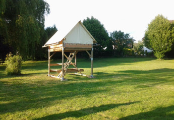Safari teltet Bivouac står på en grøn mark omgivet af træer, belyst af blødt eftermiddagslys.