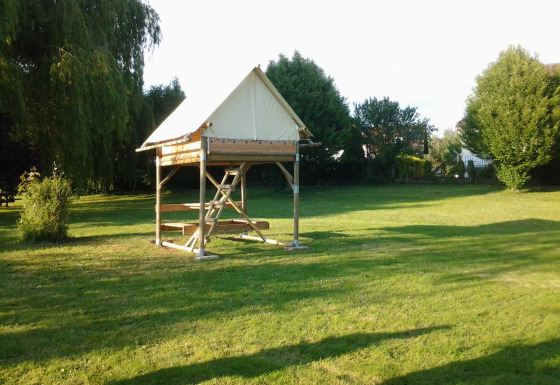 The Bivouac safari tent sits on a grassy field, surrounded by trees and basking in the afternoon sun.