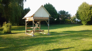 Das Bivouac-Safari-Zelt steht auf einer grünen Wiese, umgeben von Bäumen und Sonnenschein.