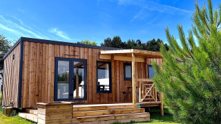 Moderne træhytte i solskin med terrasse og have, set foran Cottage Prestige-lodgen under blå himmel.