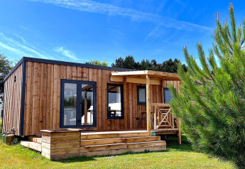 Moderne træhytte i solskin med terrasse og have, set foran Cottage Prestige-lodgen under blå himmel.
