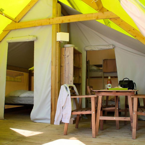 Interno di una tenda safari con tavolo da pranzo, sedie, scaffale e aree notte visibili sullo sfondo