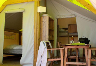 Interno di una tenda safari con tavolo da pranzo, sedie, scaffale e aree notte visibili sullo sfondo
